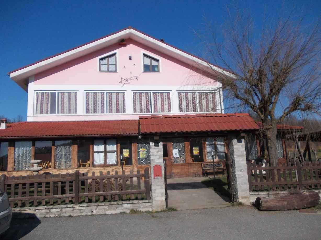 Facciata rosa di agriturismo con tetto in coppi, cancellata in legno, cielo azzurro