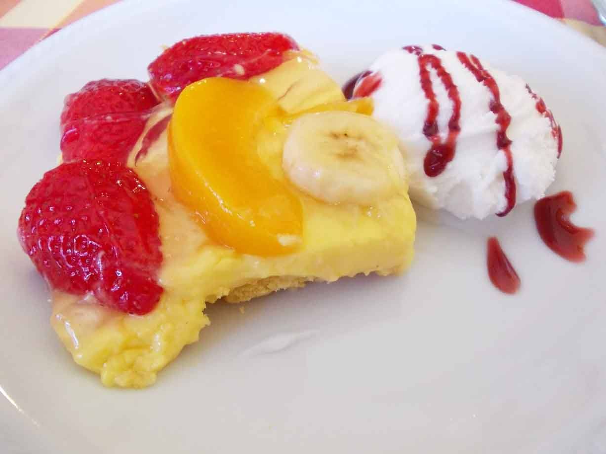 Torta della nonna con fragole, pesca e banana accanto a panna con coulis di fragole