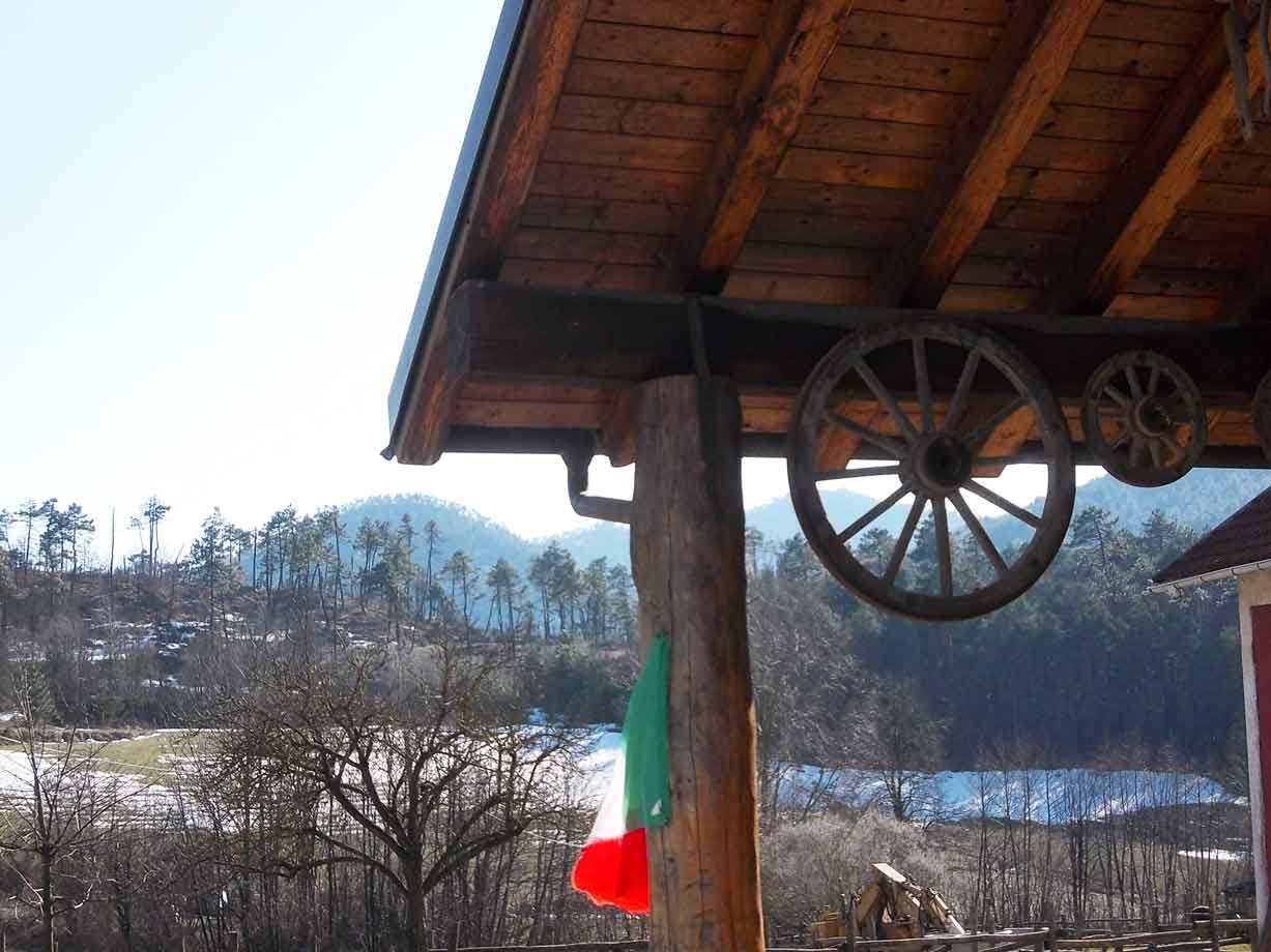 Ruote di legno appese sotto il tetto in travi, bandiera italiana, boschi con neve