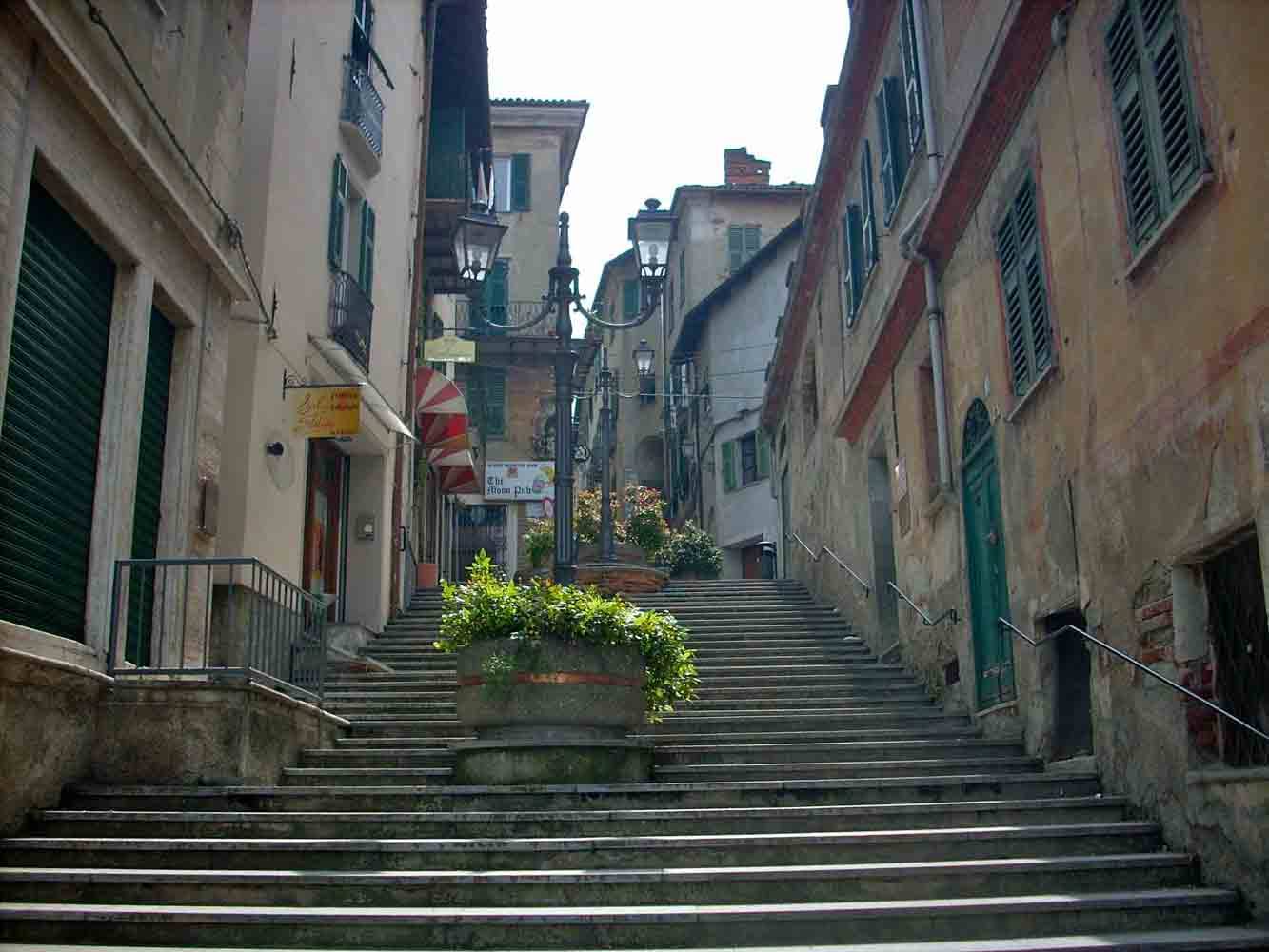 Scalinata in pietra tra case vecchie con persiane verdi, lanterne e fiori