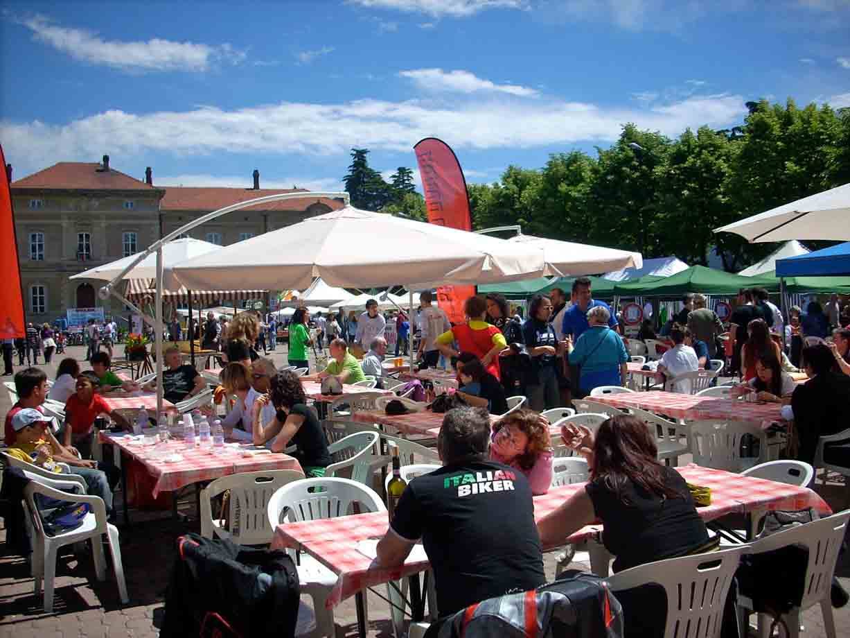 Ombrelloni e tavoli con tovaglie a quadri in piazza affollata sotto il sole