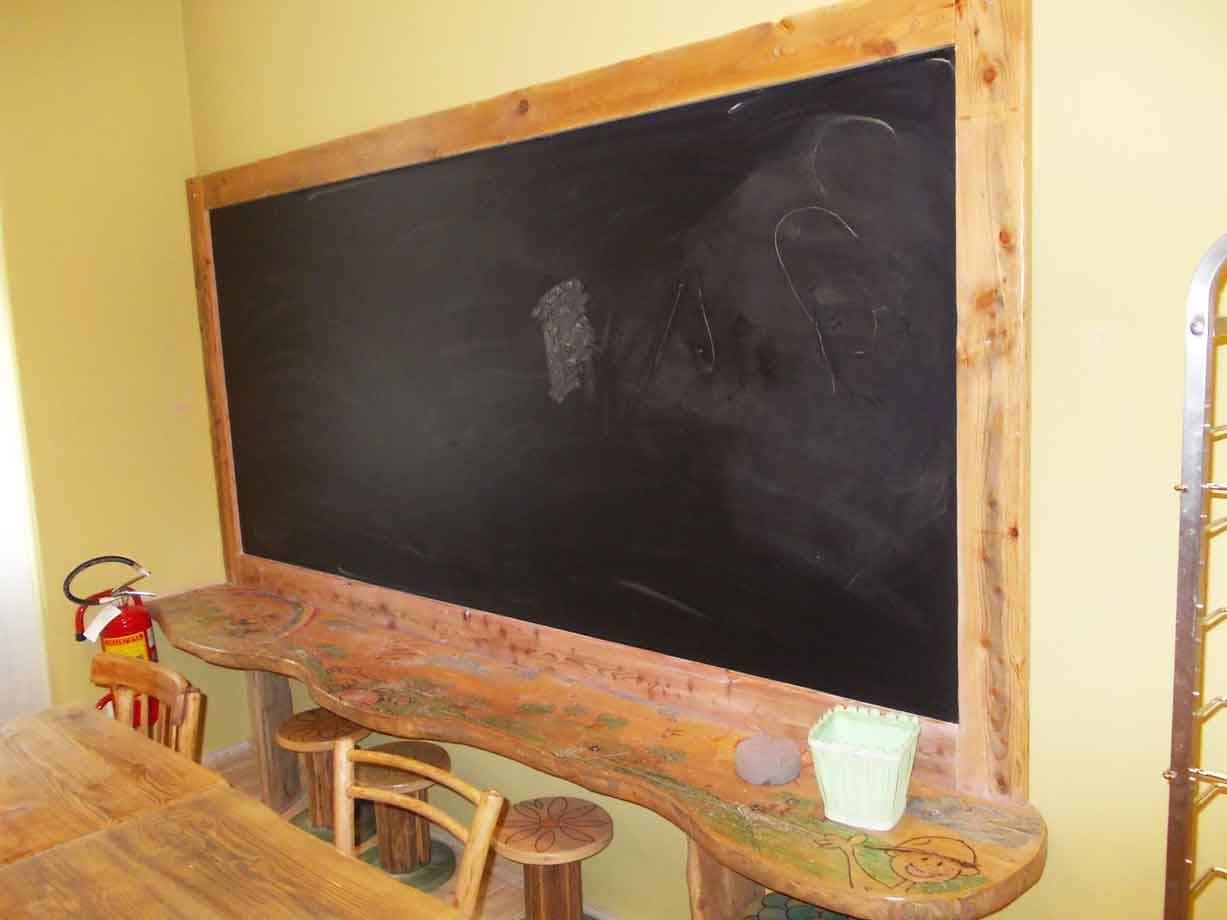 Lavagna nera con cornice di legno massello sopra un bancone scolpito, sgabelli e estintore
