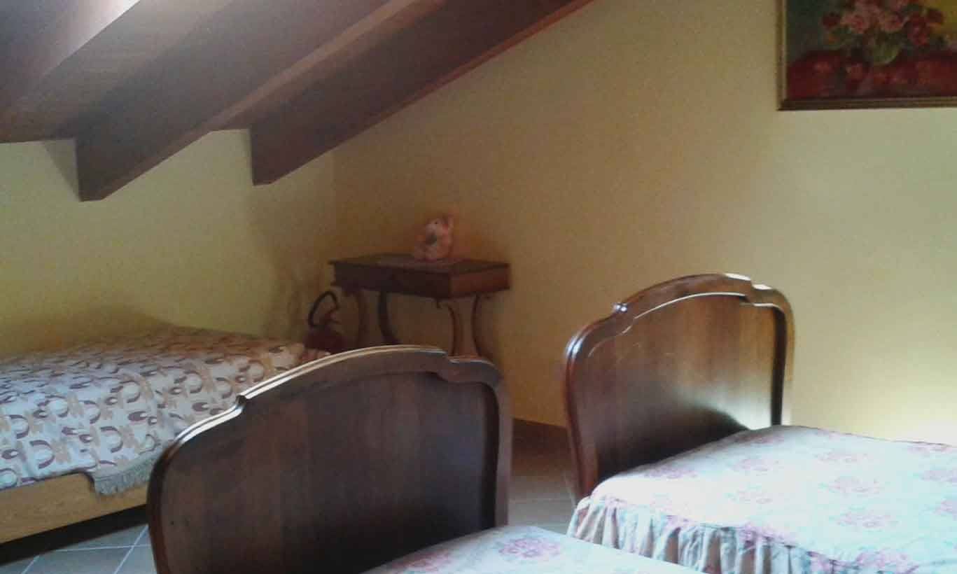 Camera sottotetto con due letti in legno scuro, luce soffusa, quadro con fiori