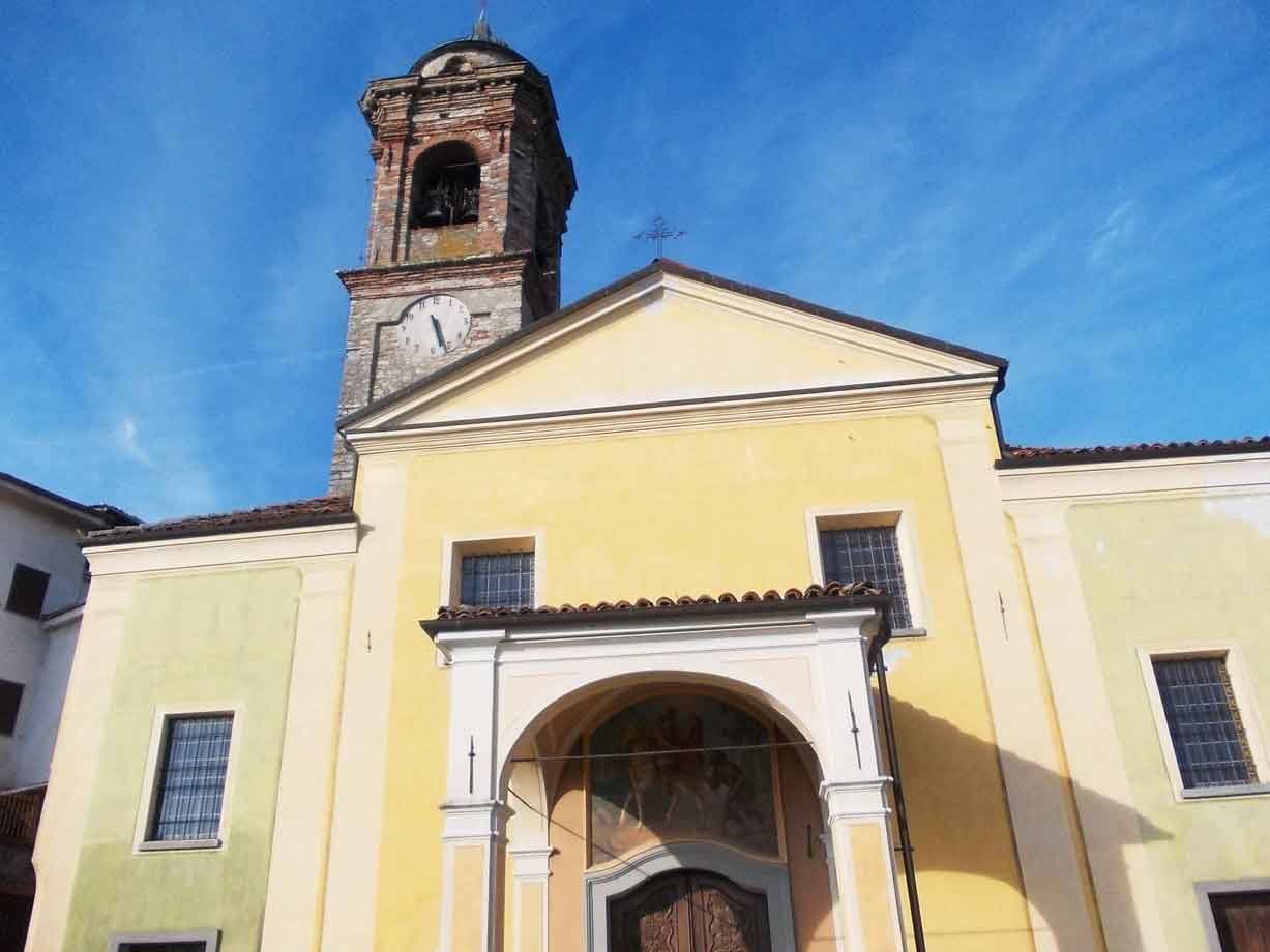 Facciata gialla della chiesa con portico affrescato e campanile in pietra
