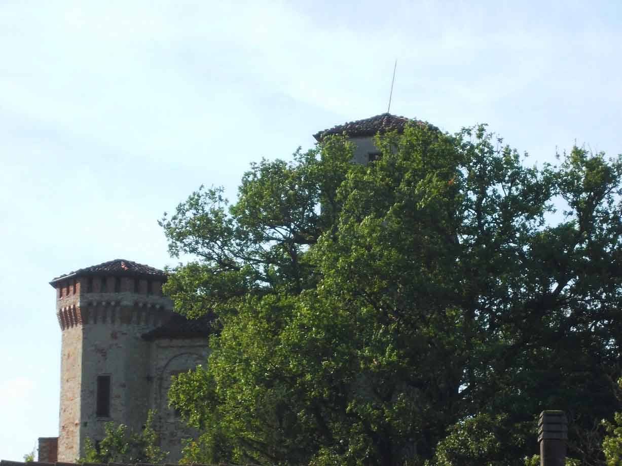 Torri in mattoni di un castello antico svelate tra chiome verdi, cielo chiaro