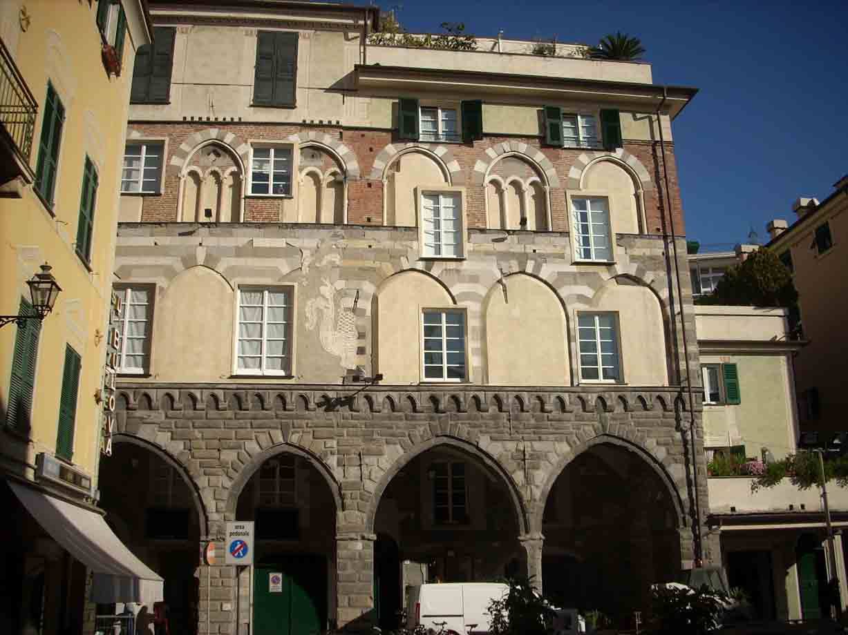 Palazzo medievale in pietra con loggiato ad archi, facciata bicroma sotto cielo azzurro