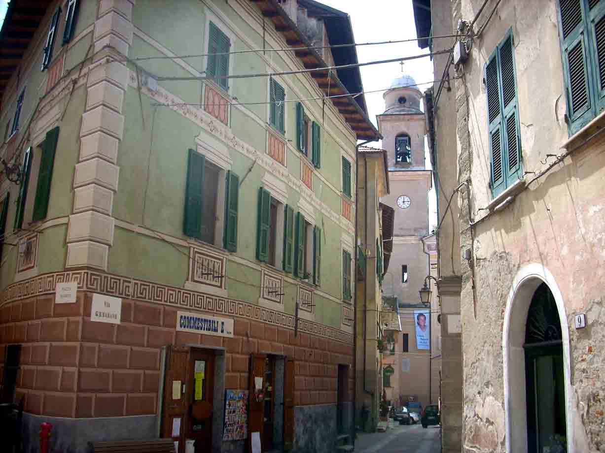 Via stretta con case affrescate e campanile con orologio sullo sfondo