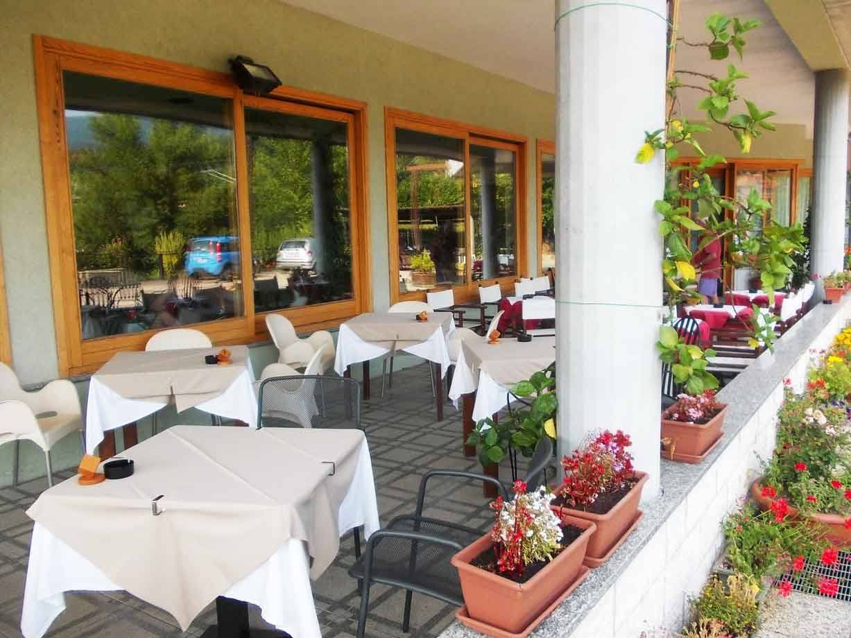 Terrazza di ristorante con tavoli apparecchiati, tovaglie bianche e vasi di fiori rossi