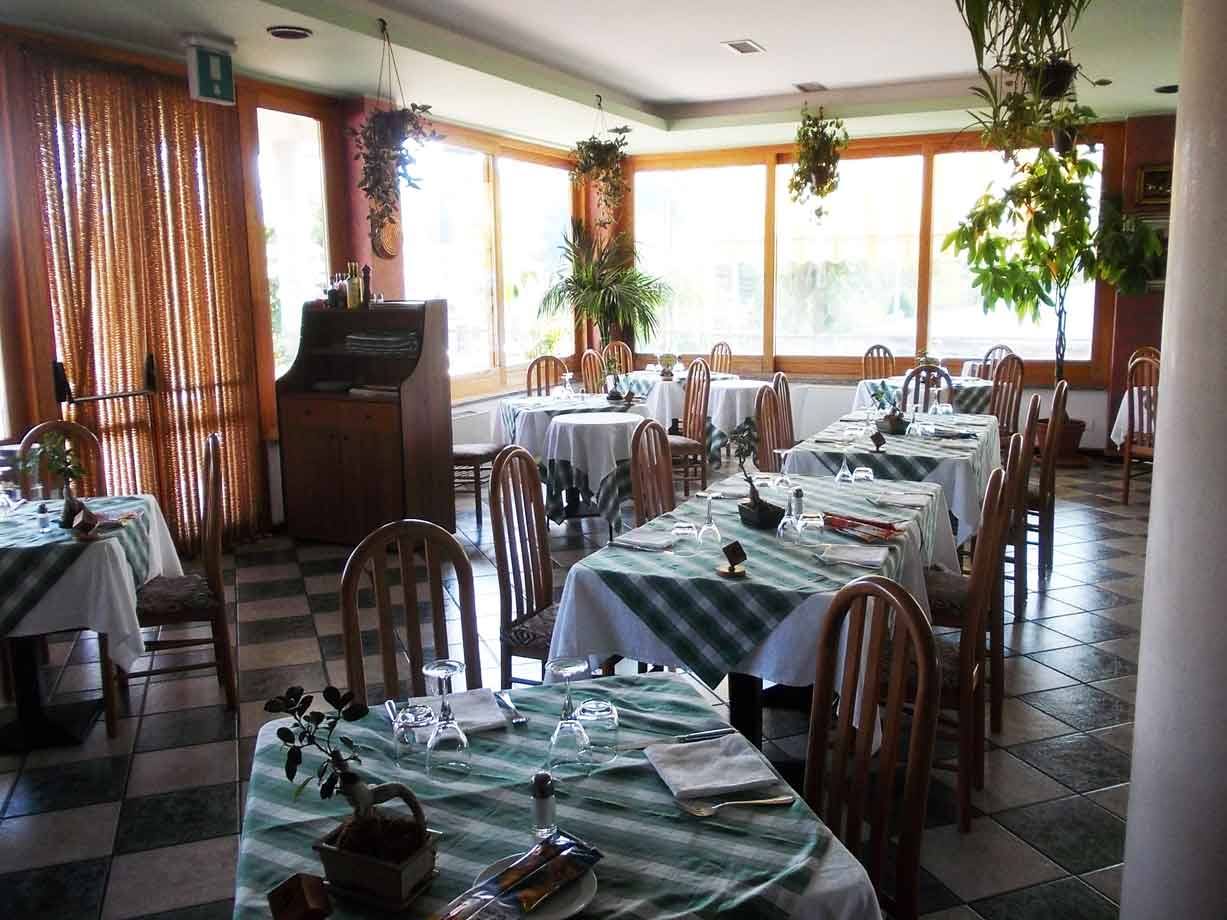 Sala di ristorante con tavoli apparecchiati, tovaglie a quadri verdi e piante appese