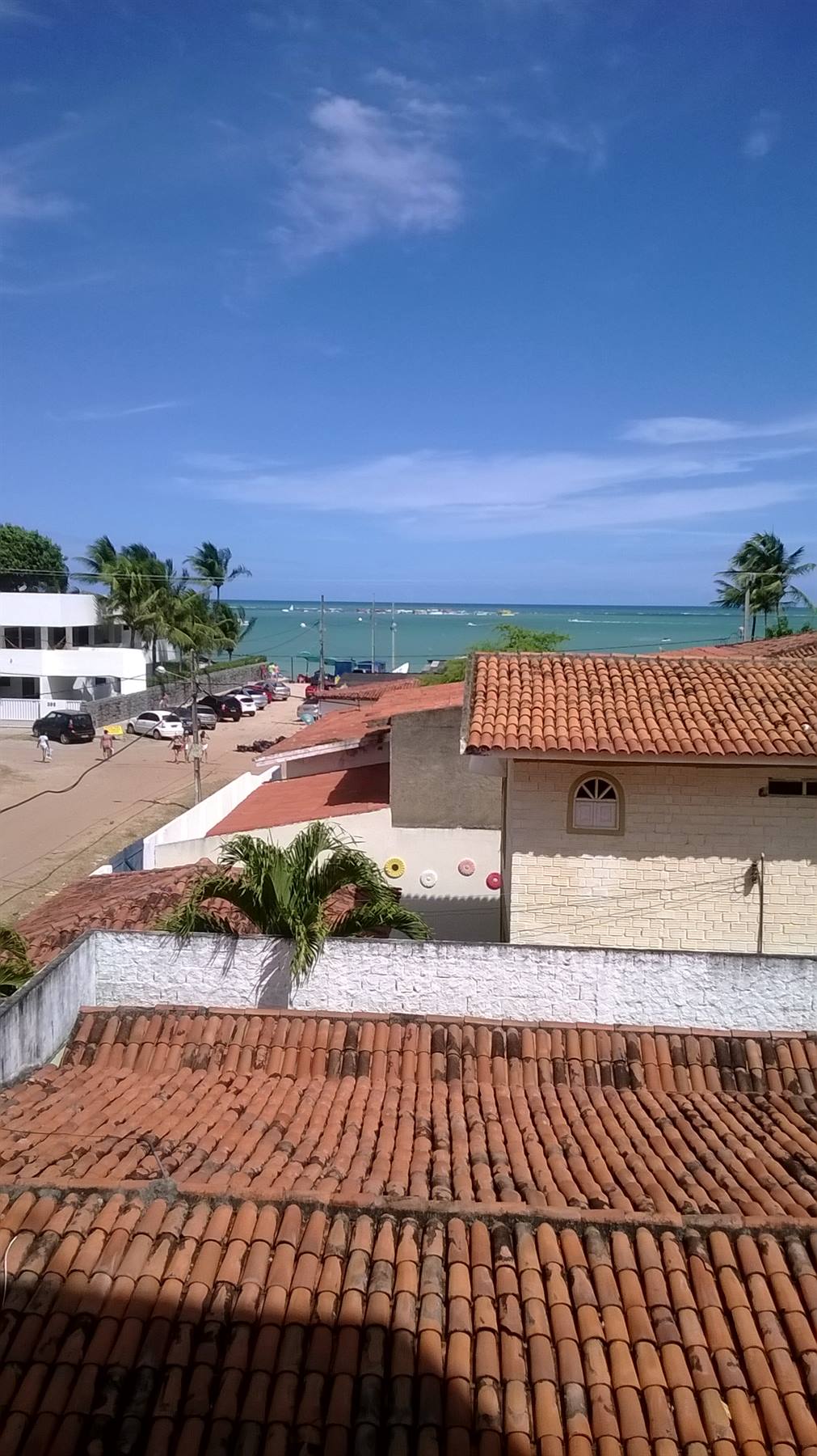 Tetti di tegole rosse davanti al mare turchese con palme e case bianche