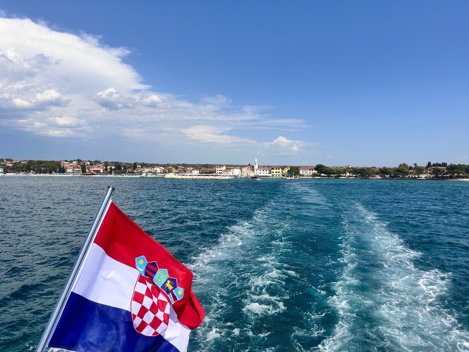 Addio alla costa istriana: la scia del traghetto e la bandiera croata al vento.